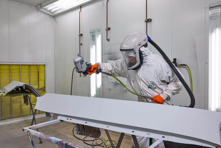 Student in protective gear painting car parts