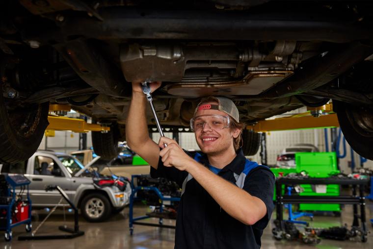 Student standing under car holding a socket wrench