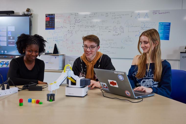Three students programming a robotic arm