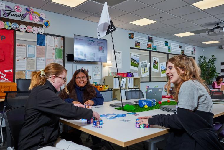 Three students playing a game with cards and blocks