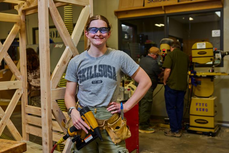 Student holding nailgun standing in front of wooden structure