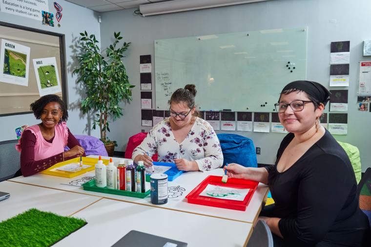Three students coloring a picture of a flower with paint