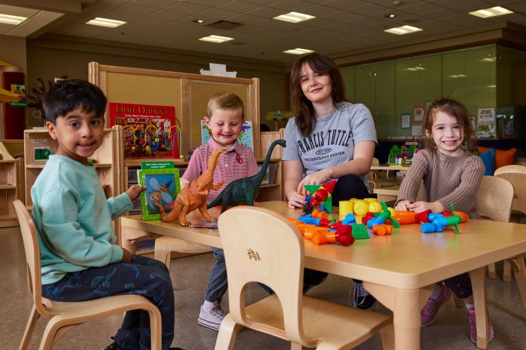 A student and three kids sitting at a table with a variety of toys