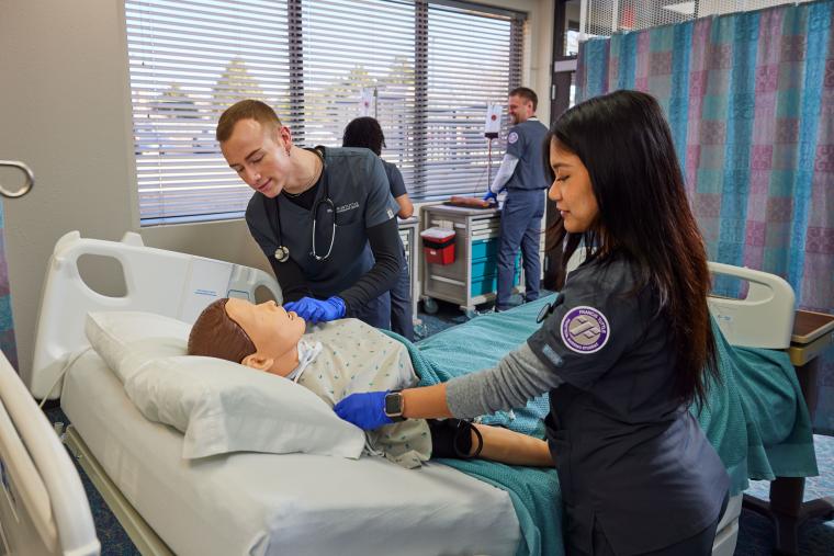 Two students attending to a mannequin in a model hospital room