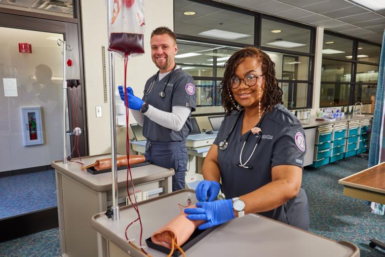 Two students practicing blood transfusions on a dummy arm