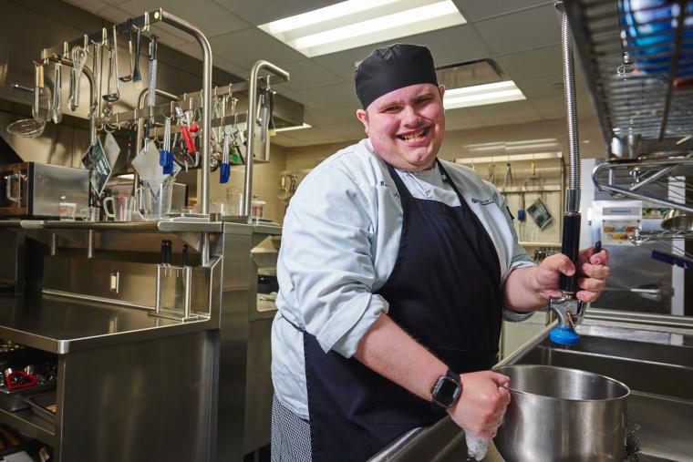 Student washing cookware in a commercial kitchen
