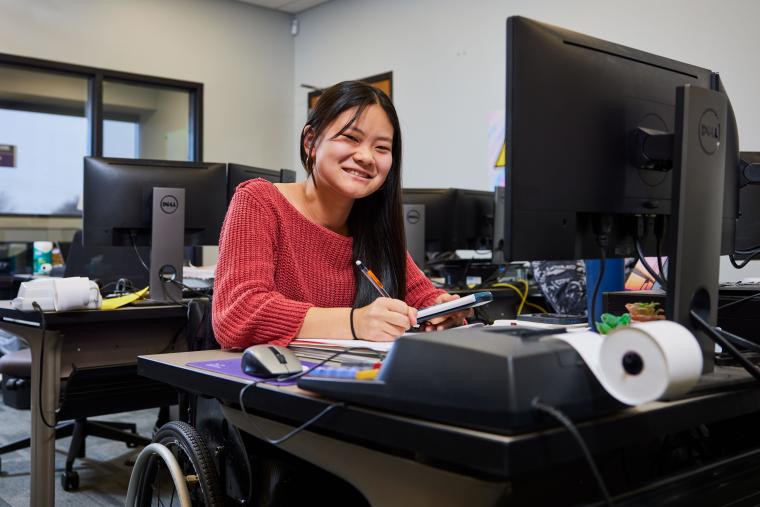 Student taking notes while holding calculator