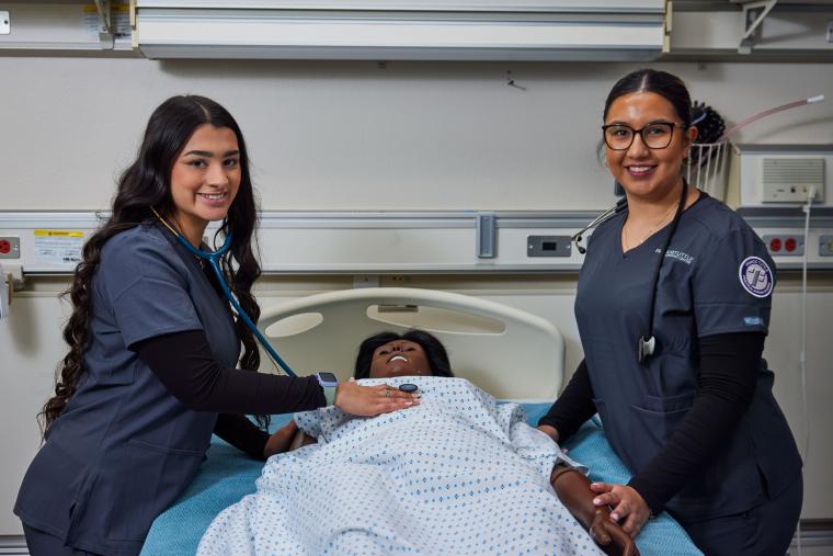 Two students checking a mannequin's heart rate with a stethoscope