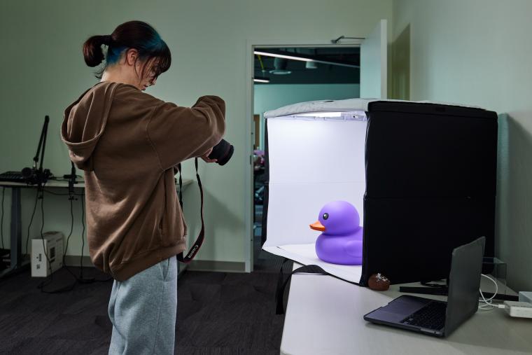 Student taking a picture of a large purple duck in a light box