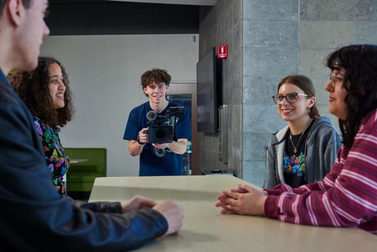 Student recording several students sitting at a table