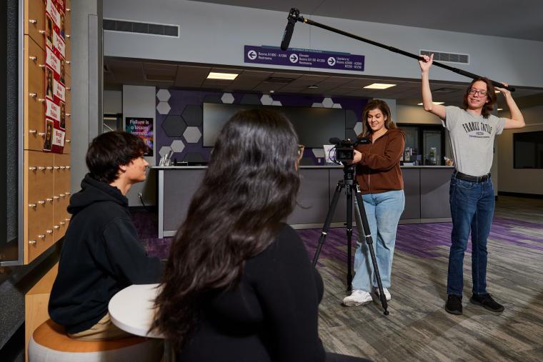 Students recording a video with a large camera and boom mic