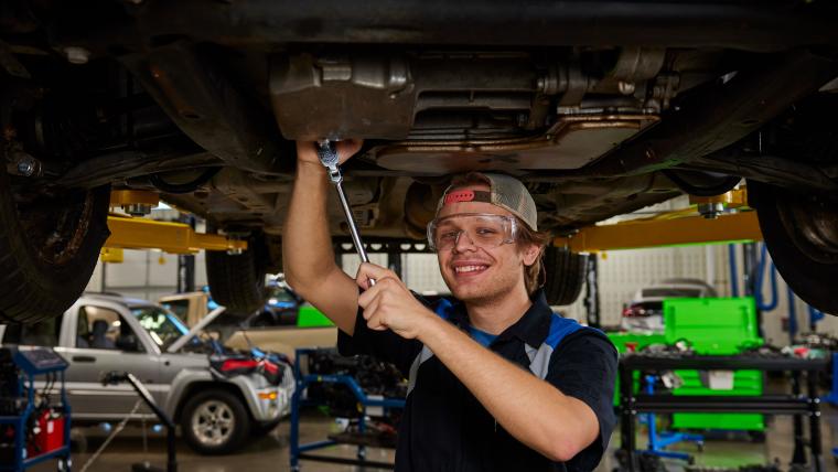 Student standing under car holding a socket wrench