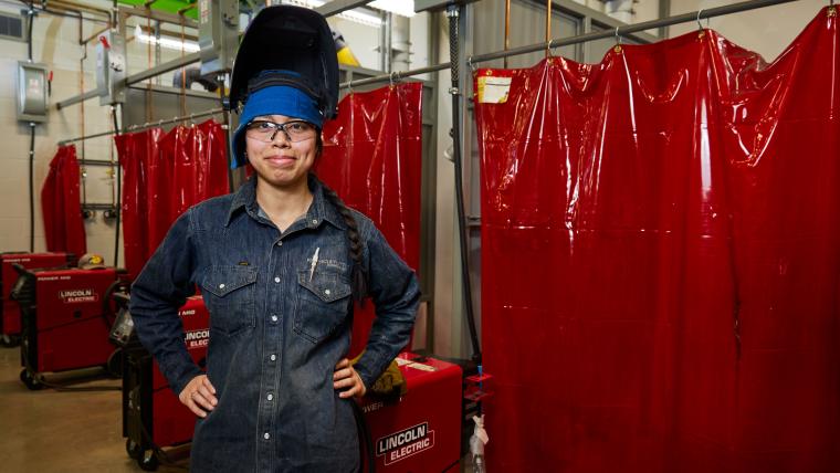 Student standing in front of several welding stations