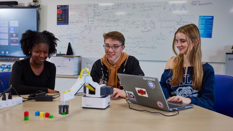 Three students programming a robotic arm
