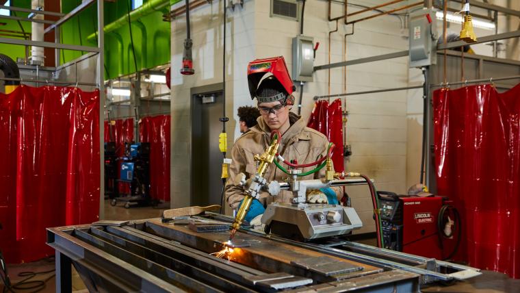 Student using a table welder to cut a steel sheet