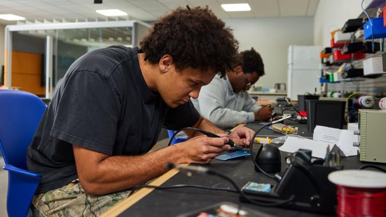 Student soldering pins on circuit board