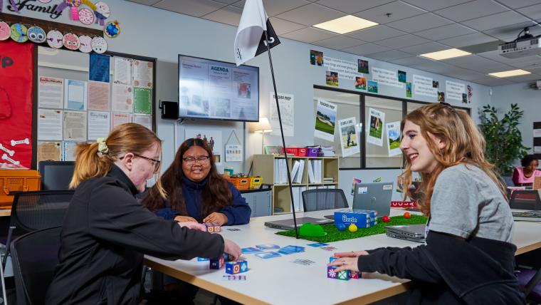 Three students playing a game with cards and blocks