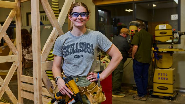 Student holding nailgun standing in front of wooden structure