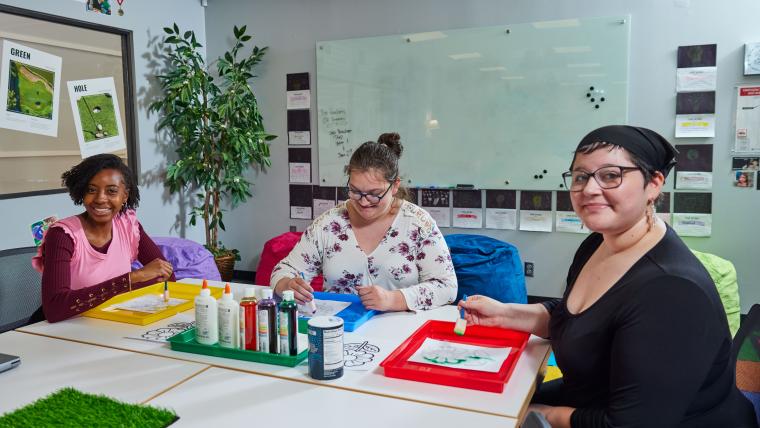 Three students coloring a picture of a flower with paint