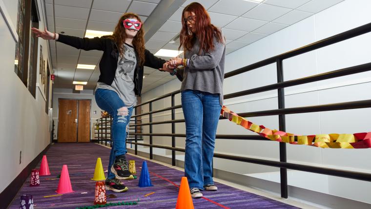 One student guiding another blindfolded student through an obstacle course