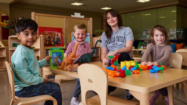 A student and three kids sitting at a table with a variety of toys