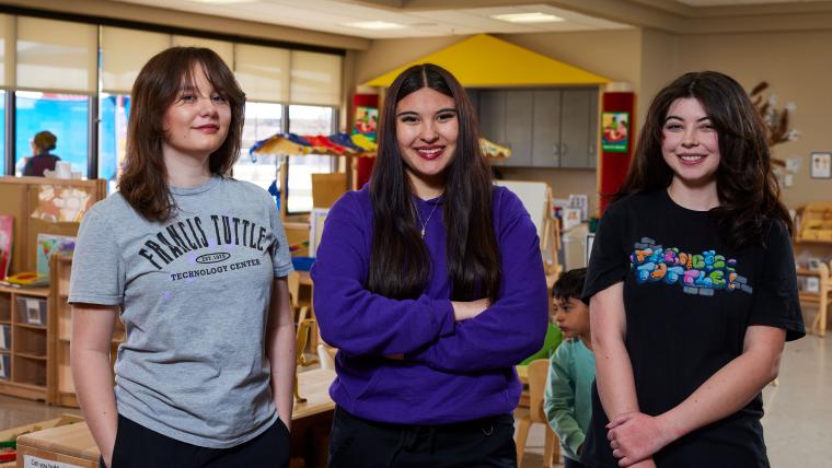 Three students standing together in the early childhood development classroom