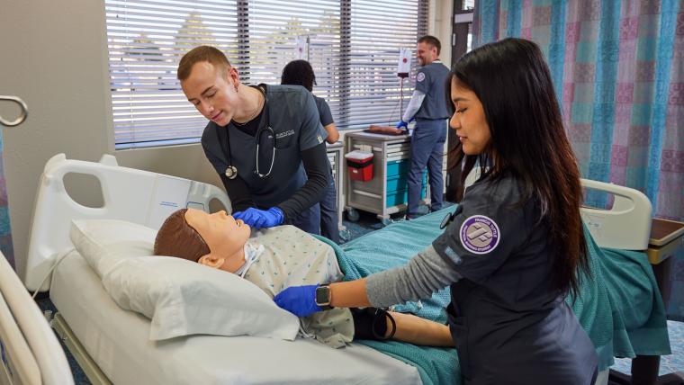 Two students attending to a mannequin in a model hospital room