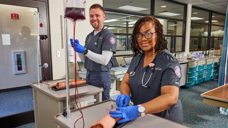 Two students practicing blood transfusions on a dummy arm