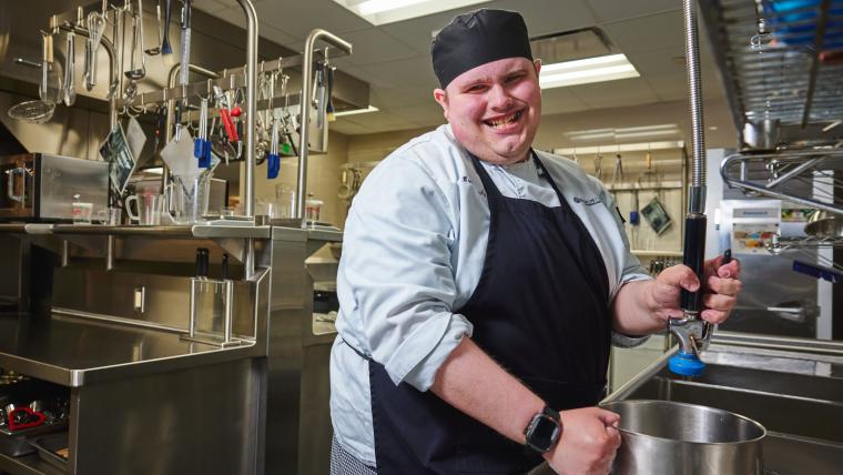 Student washing cookware in a commercial kitchen