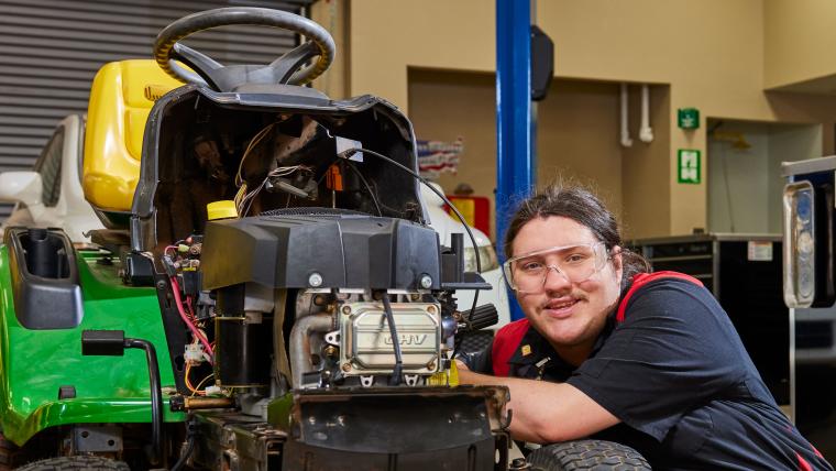 Male student working on a riding lawnmower.