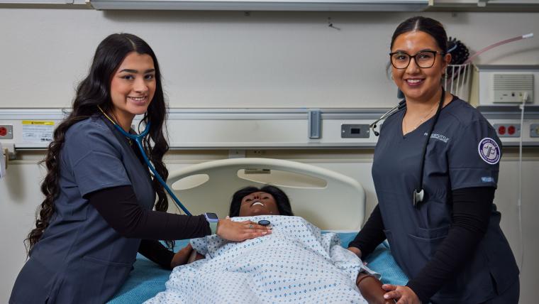 Two students checking a mannequin's heart rate with a stethoscope