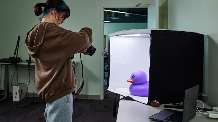 Student taking a picture of a large purple duck in a light box