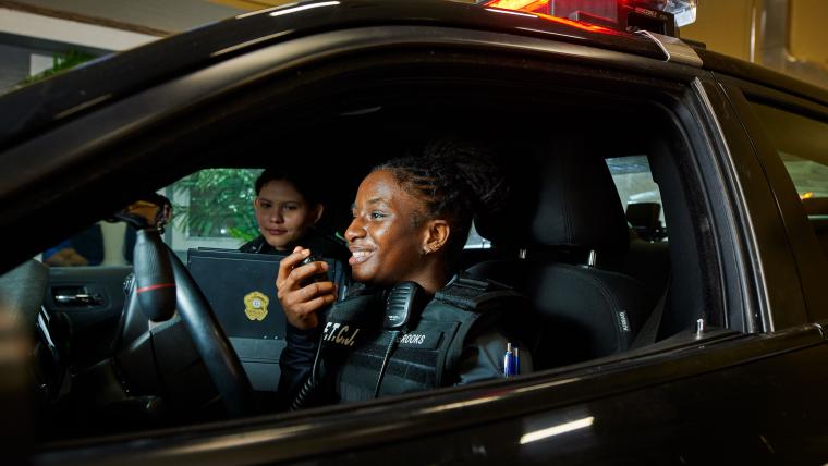 Two students practicing radio operation in a police car