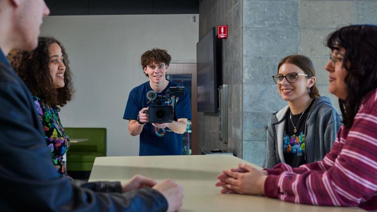 Student recording several students sitting at a table
