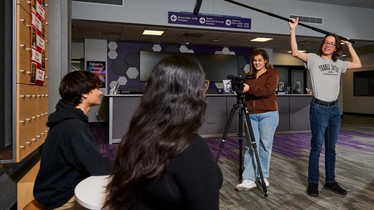 Students recording a video with a large camera and boom mic