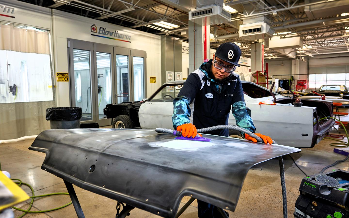 Male student sanding a car hood.