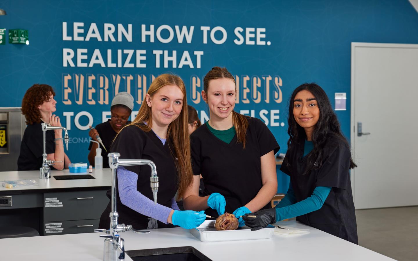 Three female students in a science lab doing a dissection.