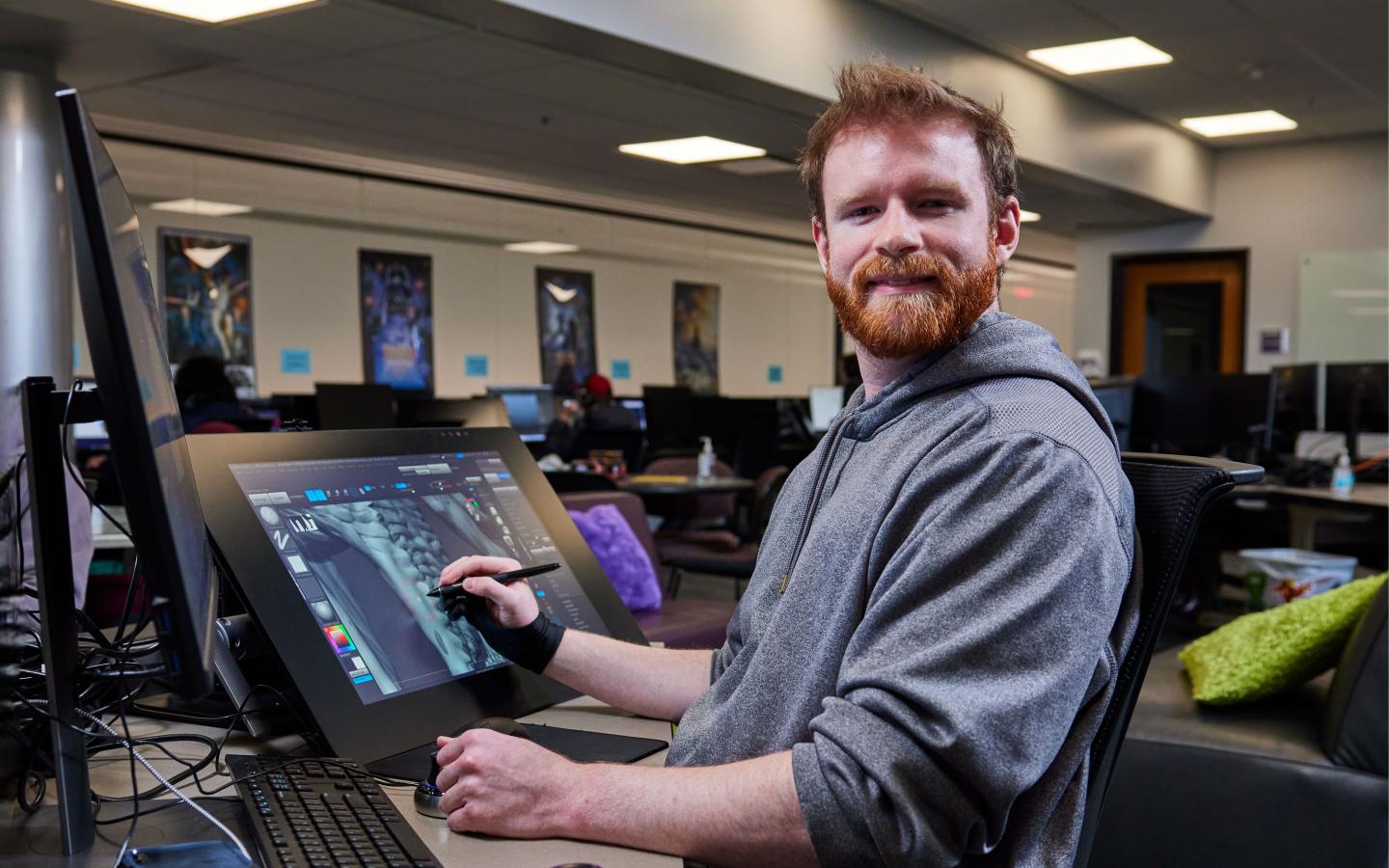 Male student sitting at a computer working on a design tablet.