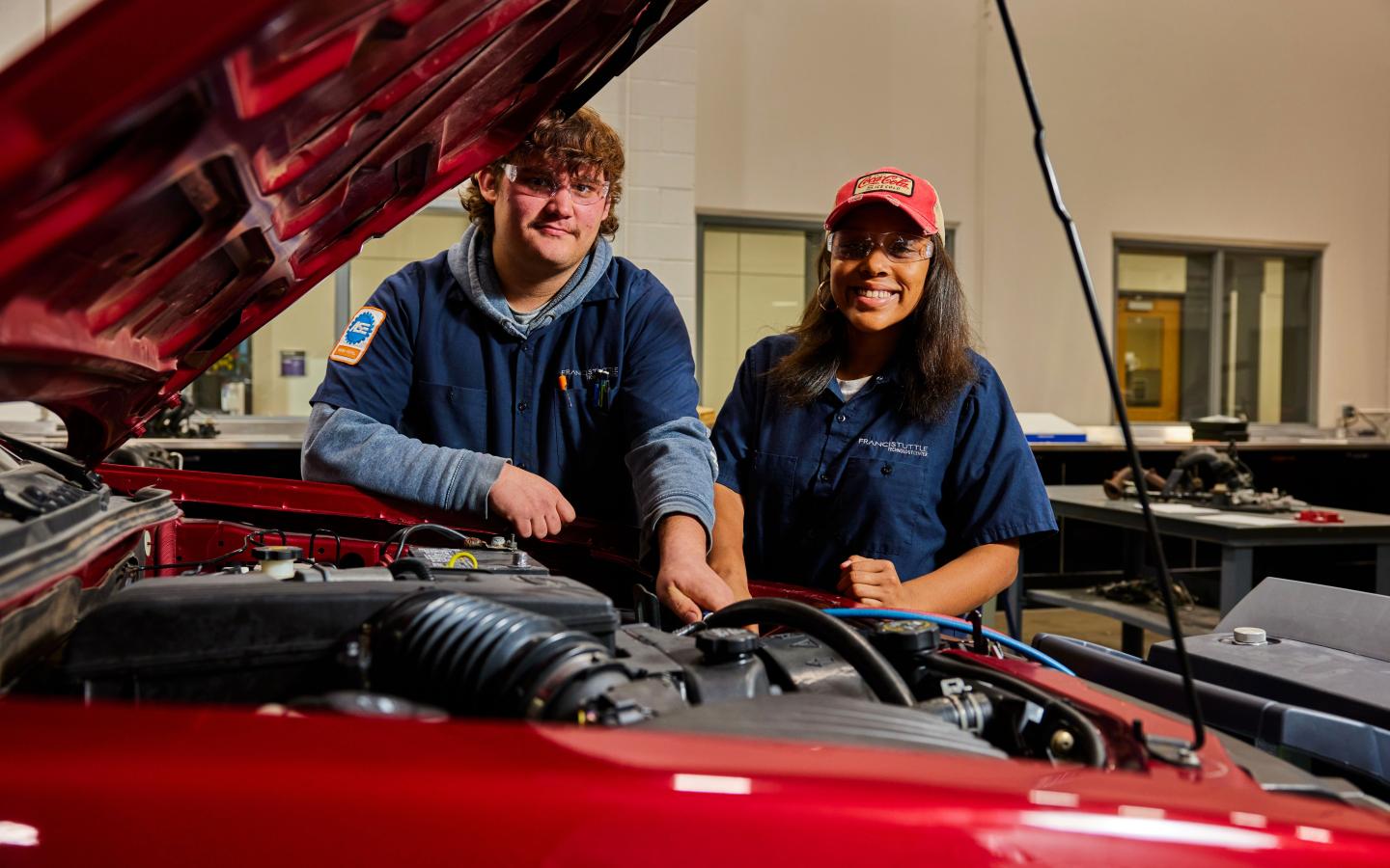 Male and female student working under the hood of a car.