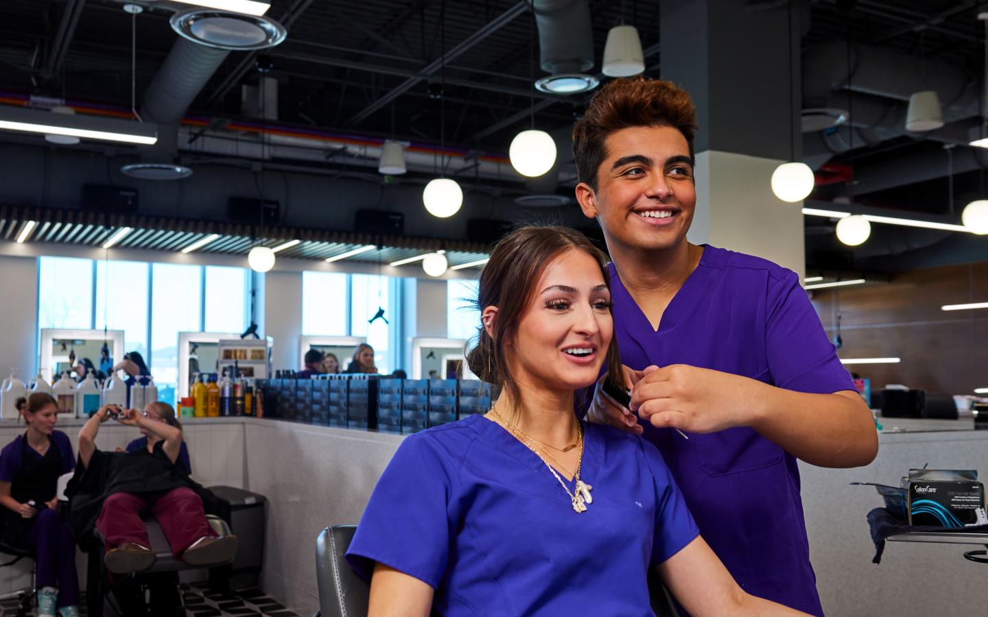 A male student working on a female student's hair.