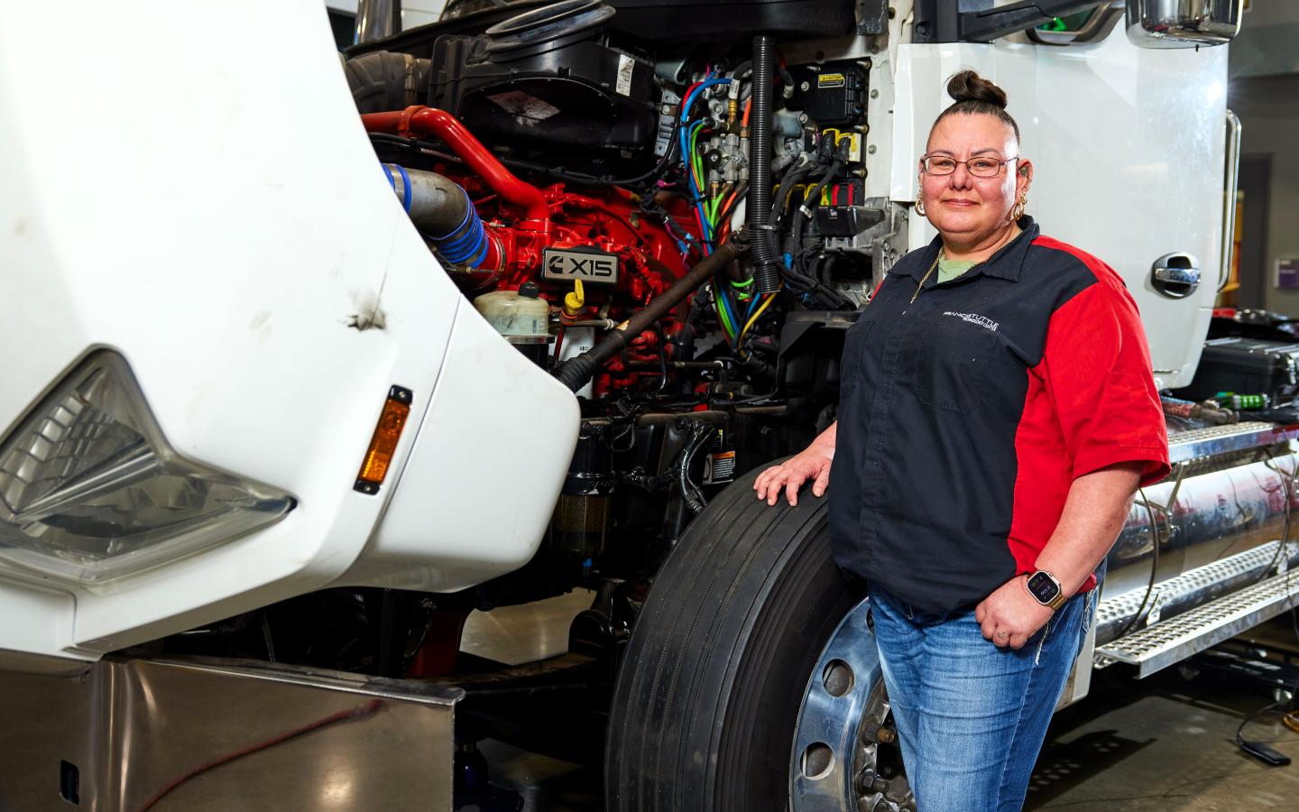 Female student standing next to a semi with the engine exposed.