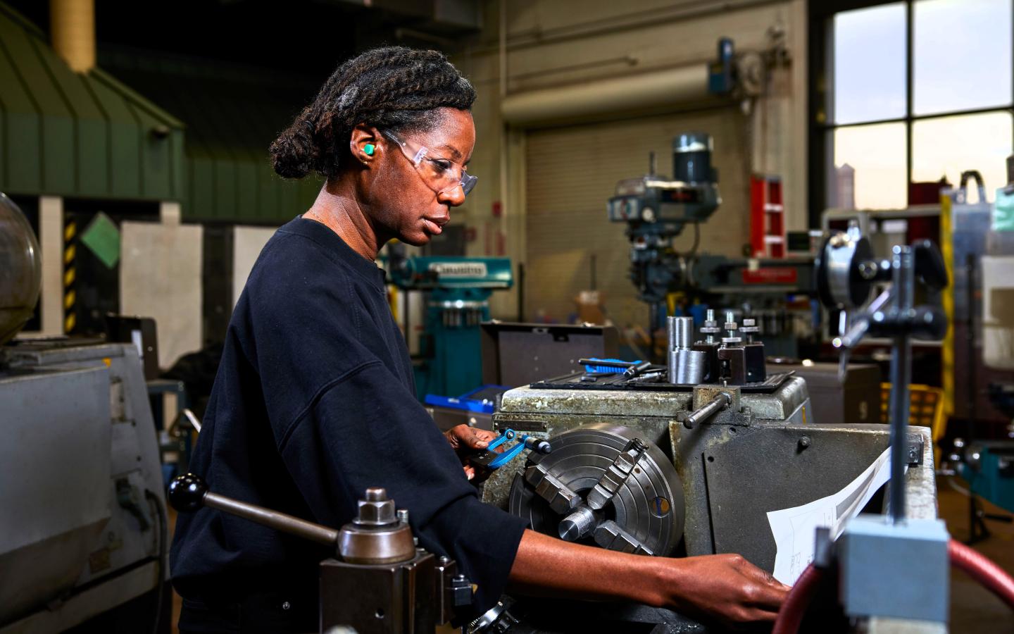 A female student working on a drill press machine.