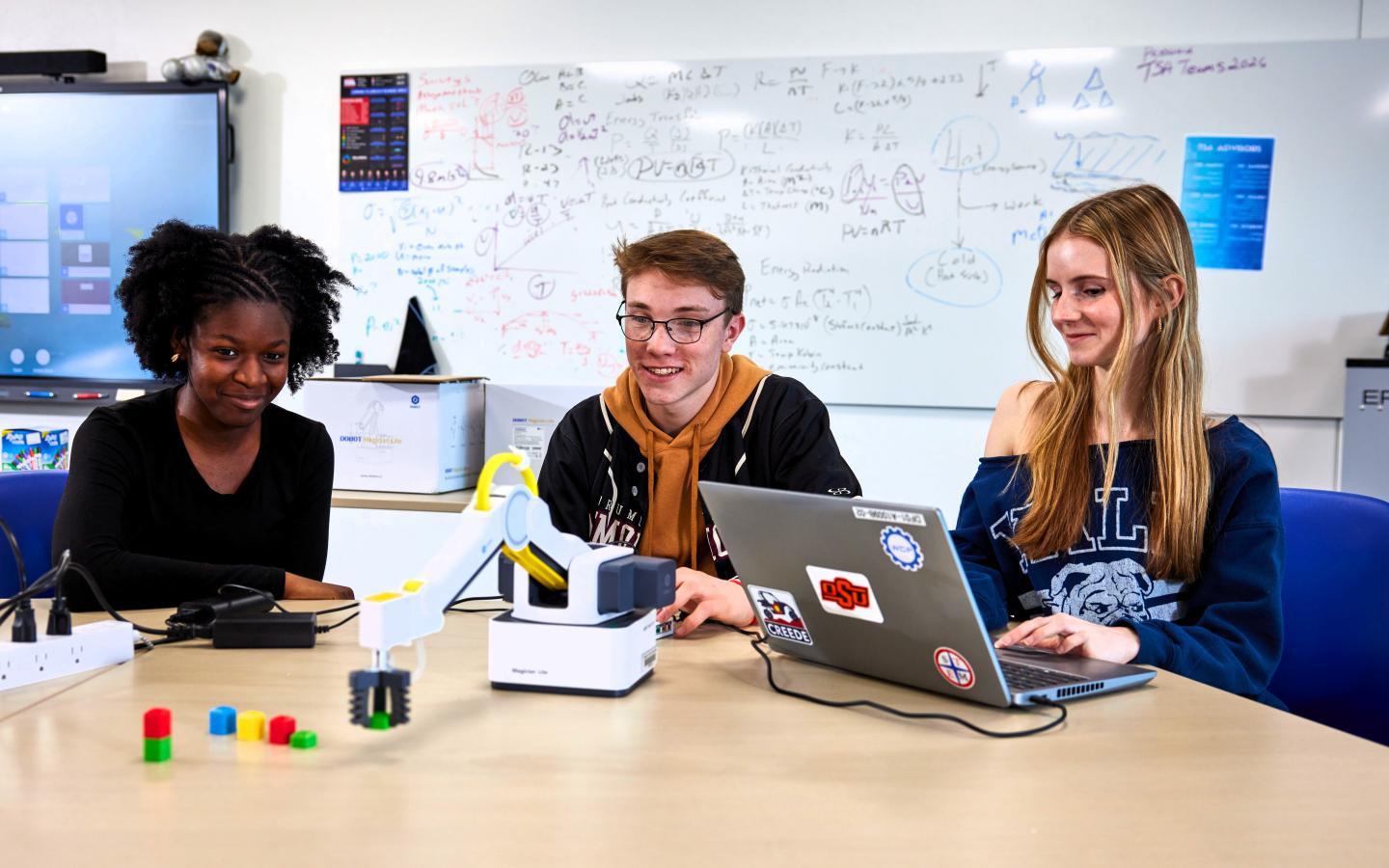 Three students working with a robotic arm.